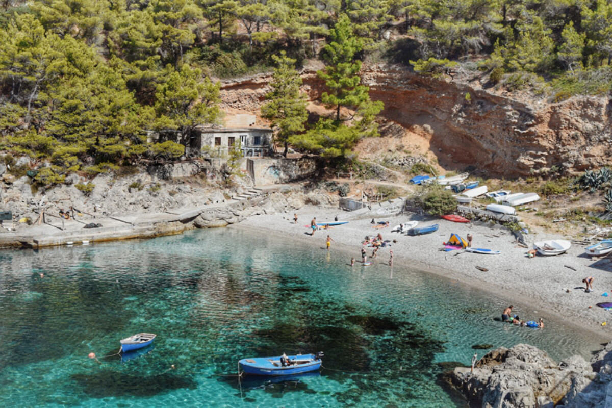 Mljet Sutmiholjska uvala i plaža Plaža Sutmiholjska na Mljetu s kristalno čistim morem, šljunčanom obalom, čamcima i borovom šumom uz crvenkaste stijene