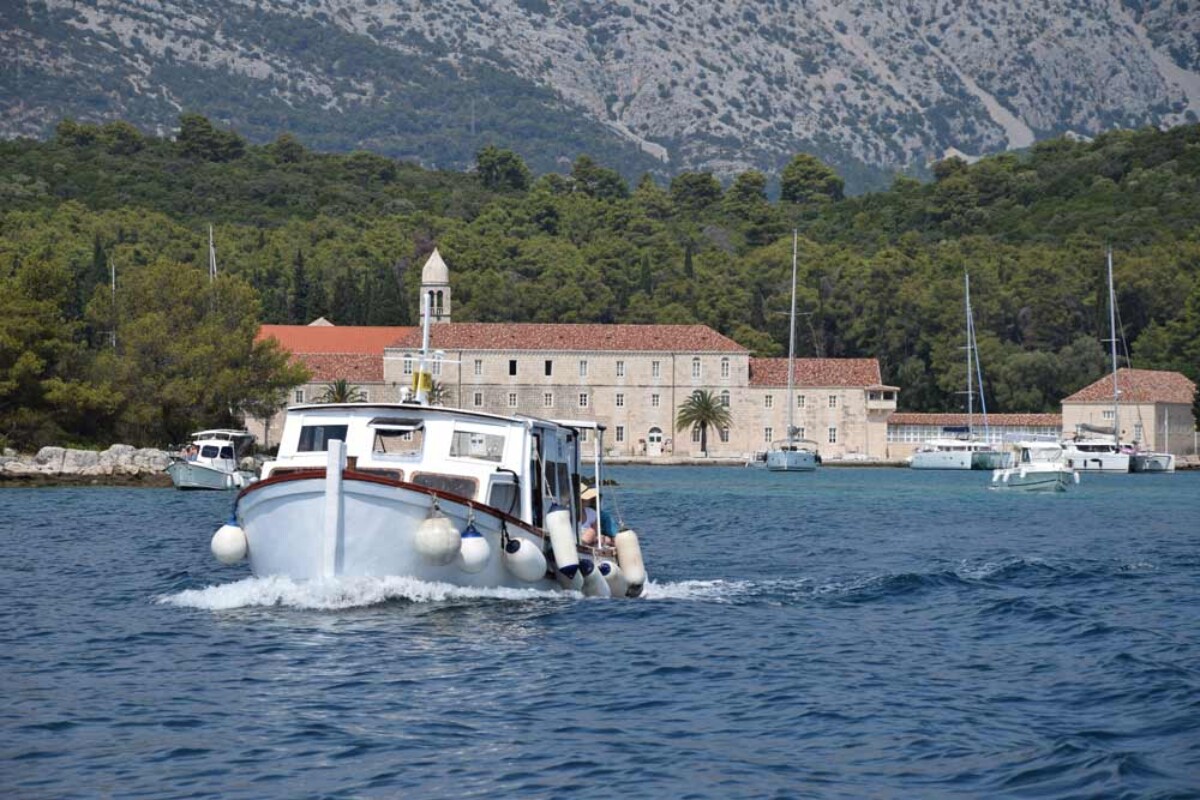 otocic-badija-i-barka Izletnički brod prilazi otočiću Badija kod Korčule, s pogledom na franjevački samostan i šumu u pozadini.