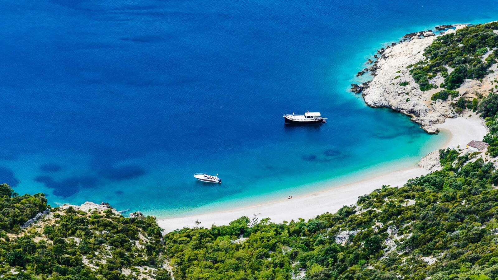 Skrivena plaža Sveti Ivan na otoku Cresu, s kristalno čistim morem, zelenilom i bijelim šljunkom u podnožju strme obale.