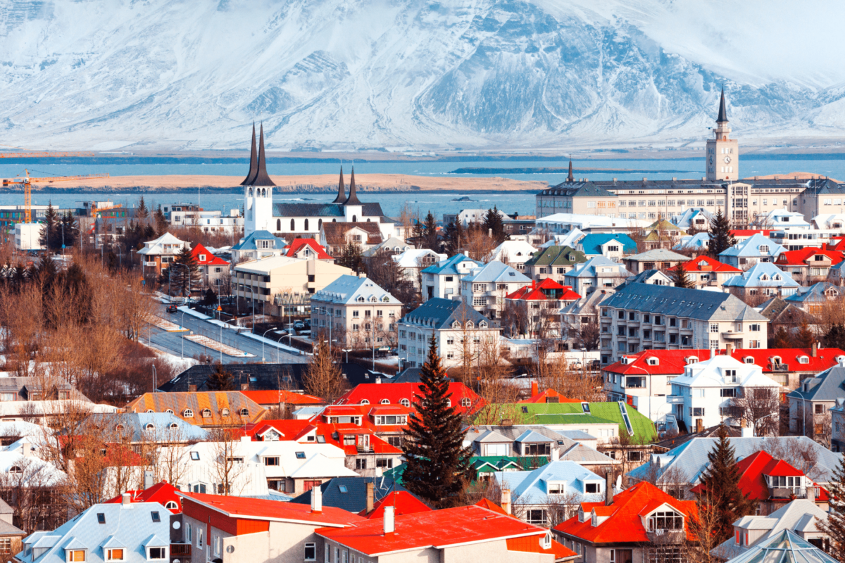 Panoramski pogled na Reykjavik, glavni grad Islanda, s raznobojnim krovovima kuća, crkvama i snježnim planinama u pozadini.