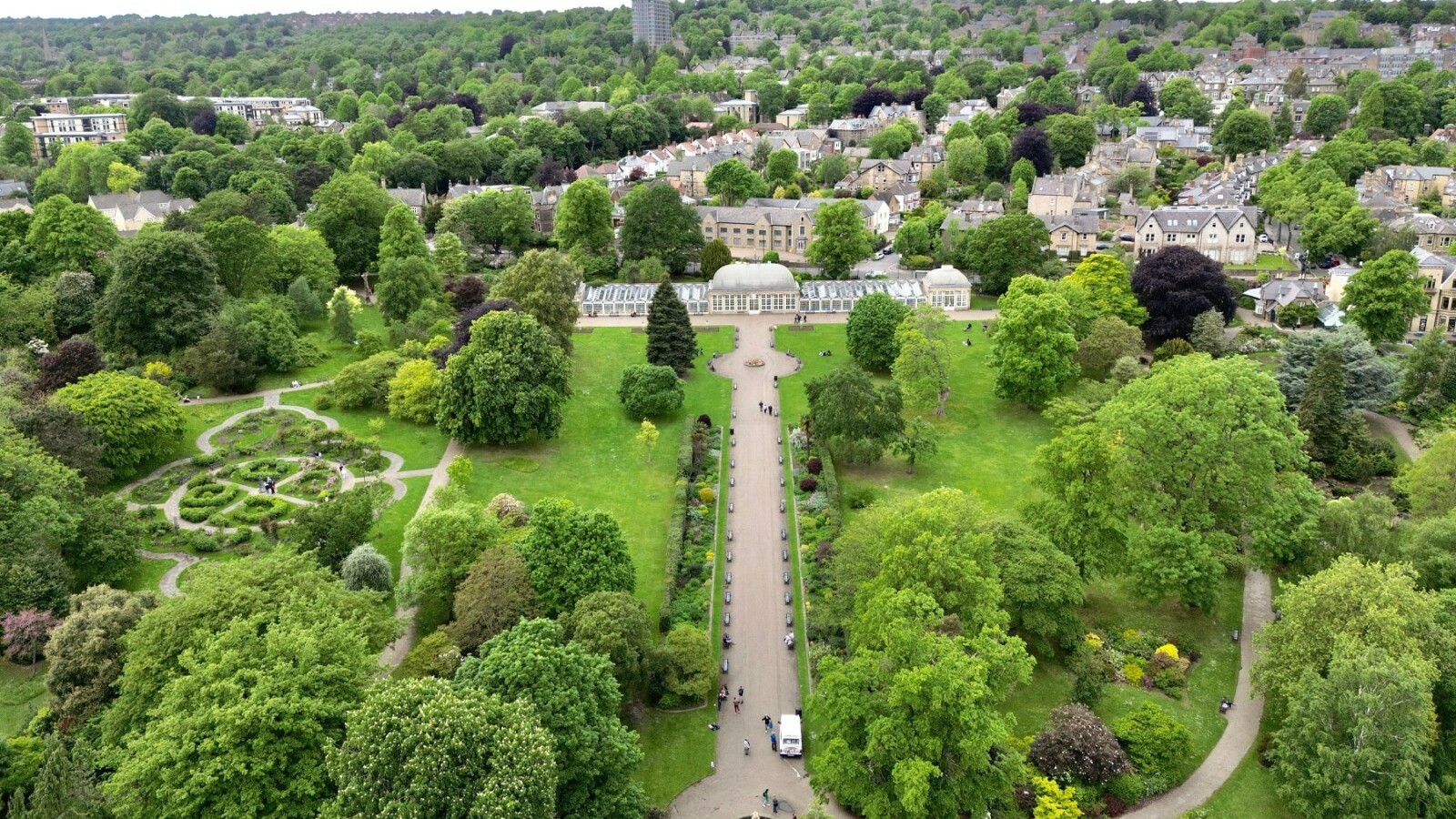 grad-sheffield-engleska Pogled iz zraka na bujni park u Sheffieldu s dugom šetnicom, fontanom i staklenikom, okruženim gustim zelenilom i stambenim četvrtima na obližnjim brežuljcima.