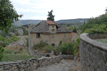 Stara kamena kuća u selu Škrip na otoku Braču s kaldrmom i kamenim zidom, okružena zelenilom i pogledom na brdoviti krajolik otoka