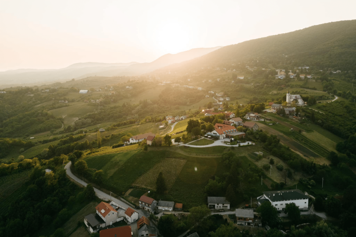 Pogled iz zraka na vinorodno područje Plešivice pri zalasku sunca, s razasutim kućama i zelenim brežuljcima