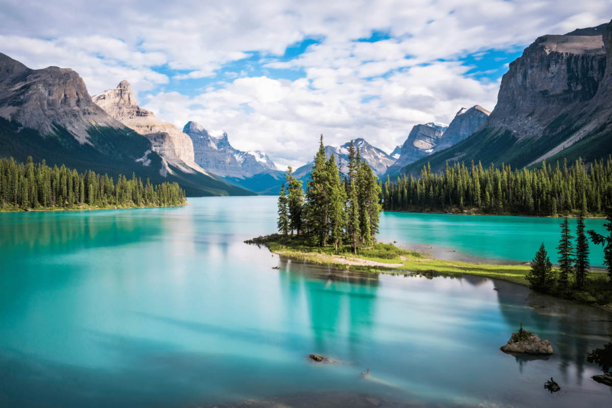 Prekrasno tirkizno jezero u Kanadi, okruženo borovim šumama i impresivnim planinama. U središtu fotografije nalazi se Spirit Island, jedno od najpoznatijih mjesta u Nacionalnom parku Jasper.