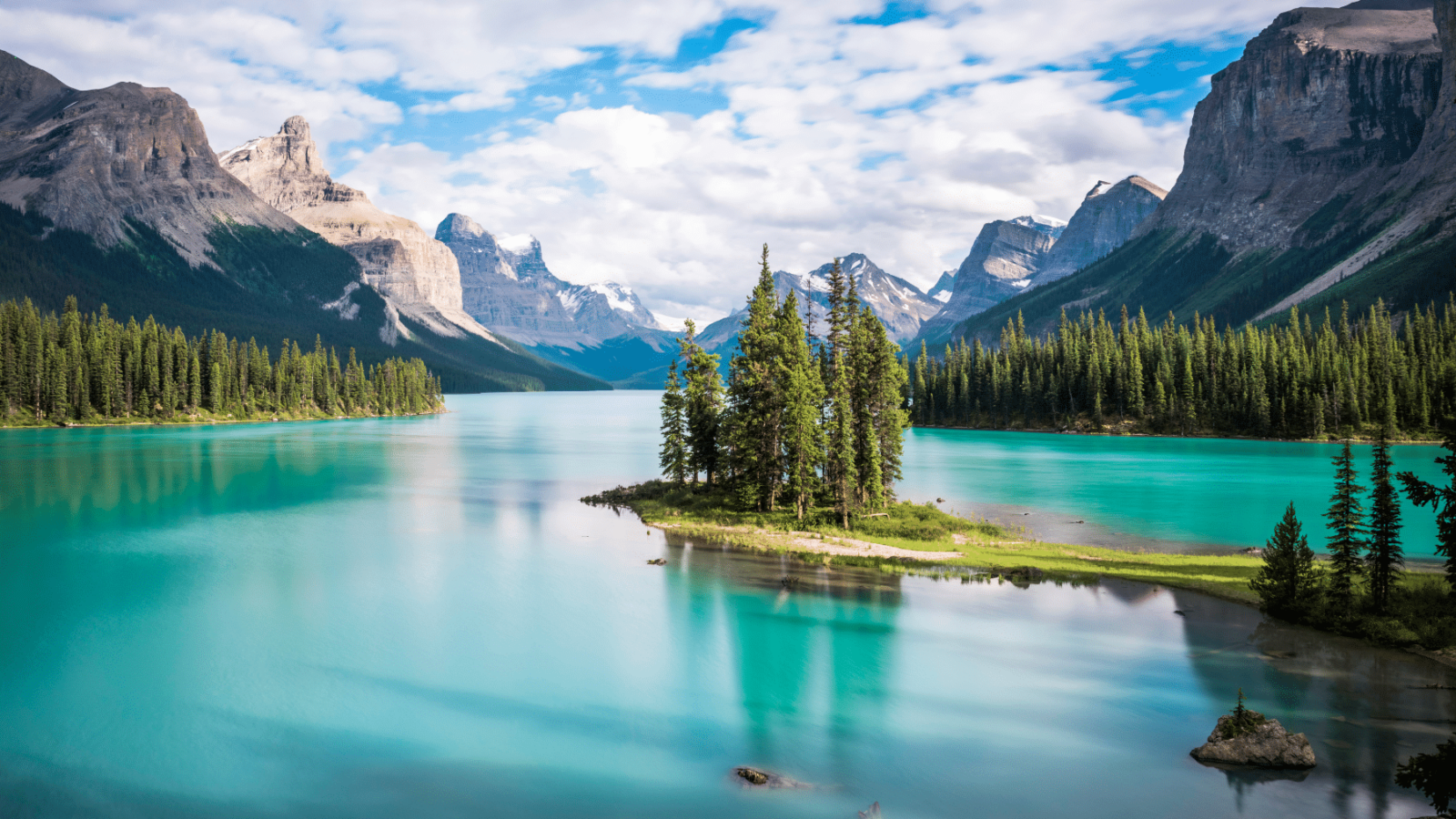 Prekrasno tirkizno jezero u Kanadi, okruženo borovim šumama i impresivnim planinama. U središtu fotografije nalazi se Spirit Island, jedno od najpoznatijih mjesta u Nacionalnom parku Jasper.