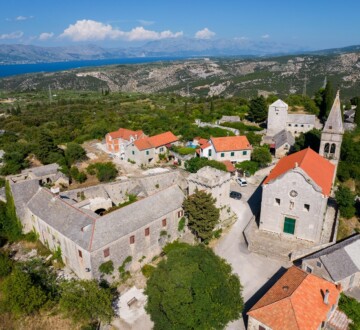 Pogled iz zraka na selo Škrip na otoku Braču s kamenim kućama, crkvom i crvenim krovovima, okruženo zelenilom i pogledom na more u daljini