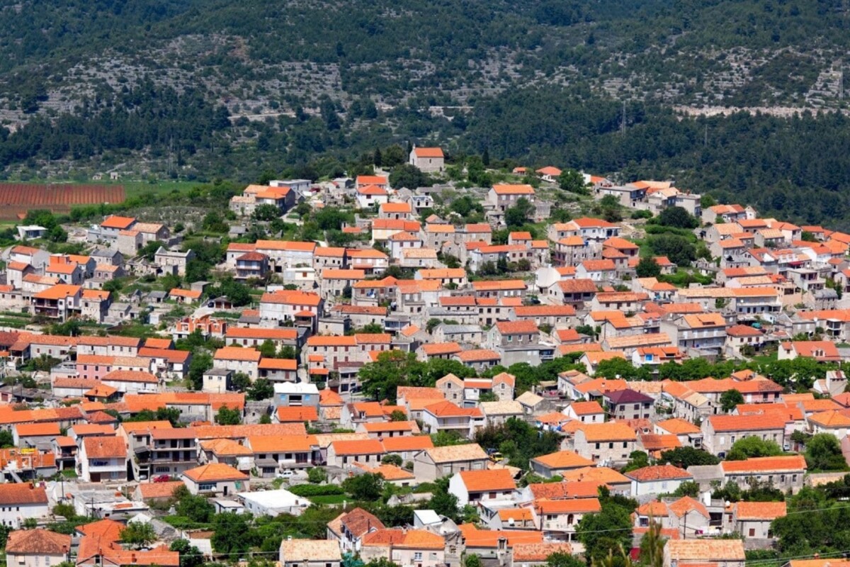blato-korcula-tradicionalne-kamene-kuce-bez-imena-ulica Tradicionalne kamene kuće s crvenim krovovima u naselju Blato na otoku Korčuli, okružene zelenilom i brdovitim krajolikom – autentični dalmatinski ambijent u srcu otoka.