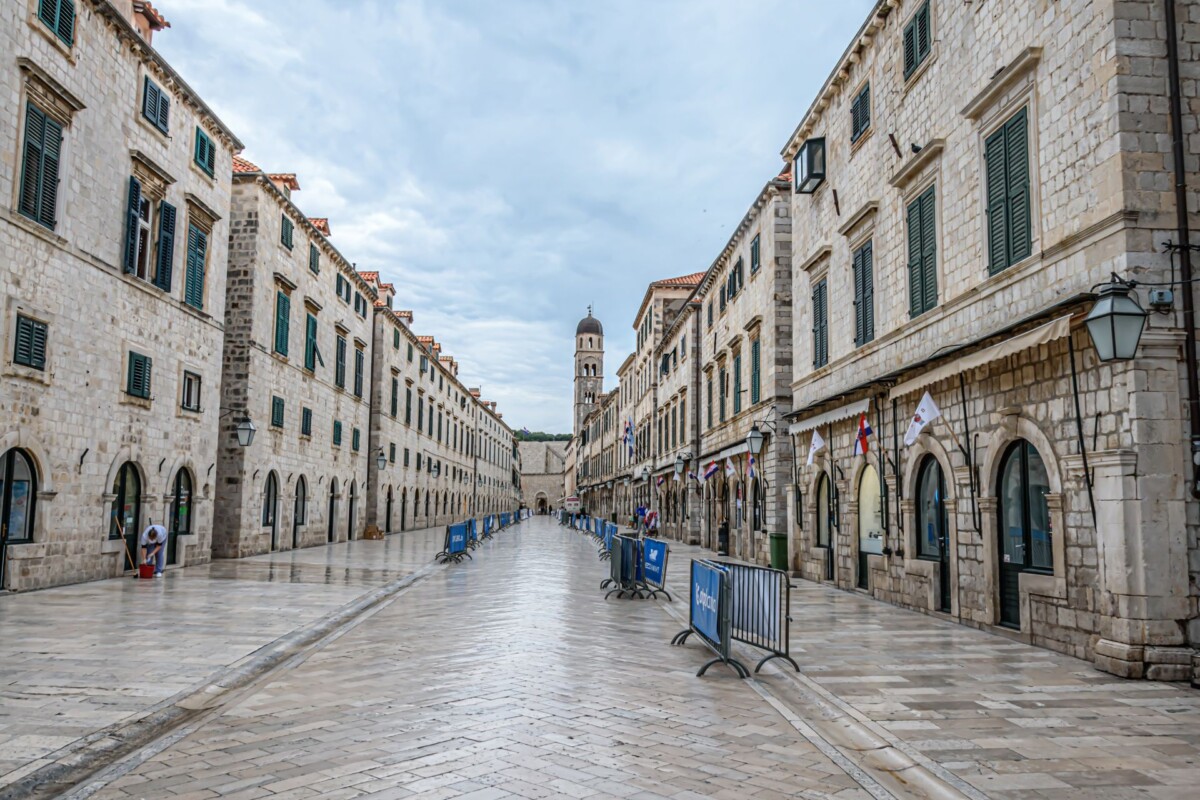 dubrovnik-stradun Pogled na Stradun, glavnu ulicu starog grada Dubrovnika, s povijesnim pročeljima i baroknim tornjem u daljini.