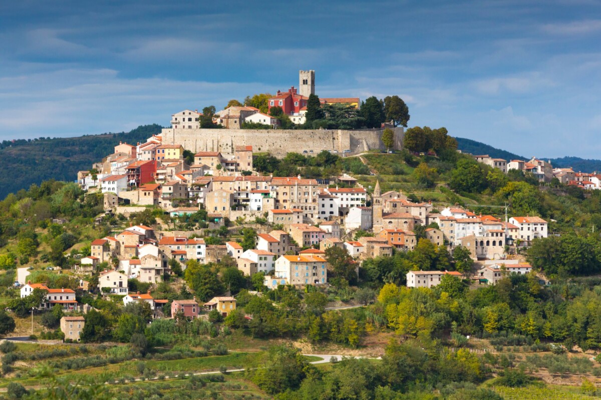Motovun, srednjovjekovni gradić smješten na brežuljku u srcu Istre, okružen zelenim krajolikom, s kamenim kućama, crkvom i zidinama koje dominiraju vrhom naselja.