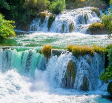 nacionalni-park-krka-skradinski-buk Slapovi Skradinskog buka u Nacionalnom parku Krka, s kristalno čistom vodom koja se prelijeva preko zelenilom obraslih stijena, okruženi bujnom vegetacijom u proljetnom okruženju.