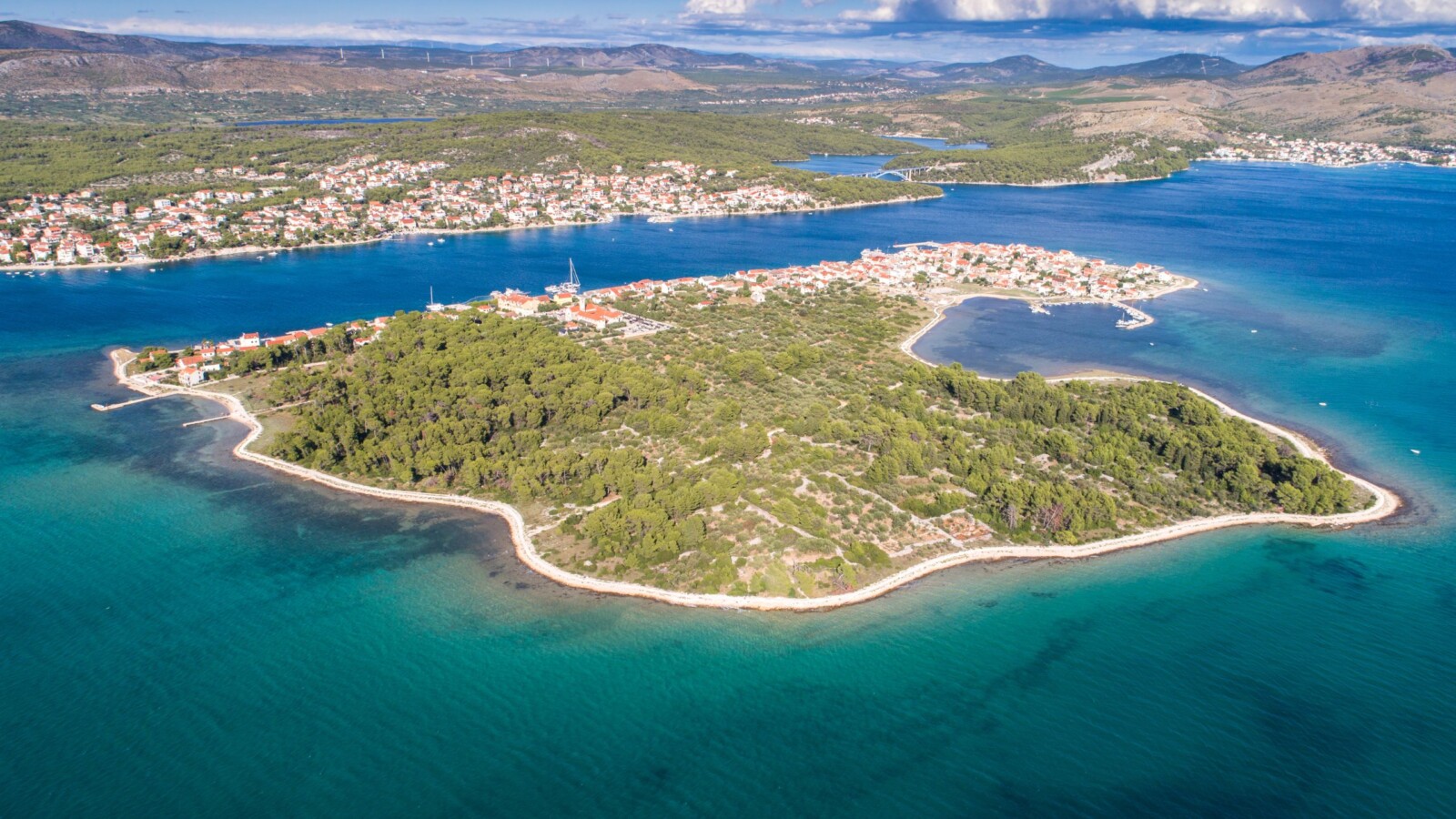 Otok Krapanj, najniži hrvatski otok, snimljen iz zraka, okružen tirkiznim morem. U daljini se vidi Brodarica