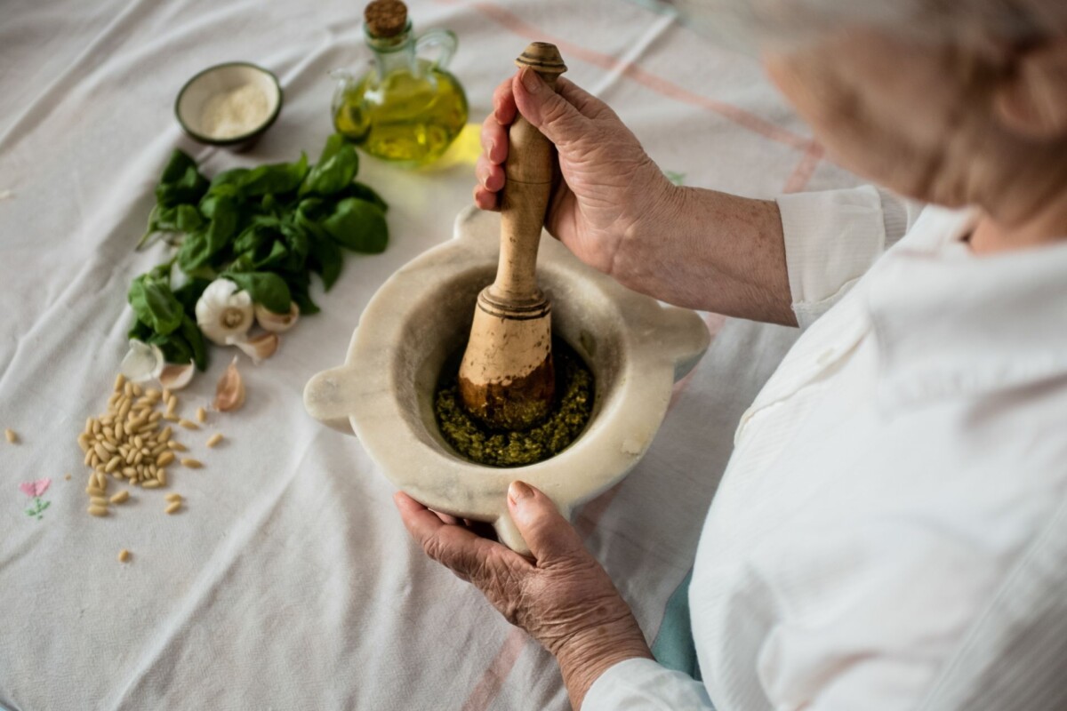 Priprema domaćeg pesto zelenog umaka u mužaru, s tradicionalnim sastojcima poput bosiljka, češnjaka, pinjola i maslinovog ulja na stolu