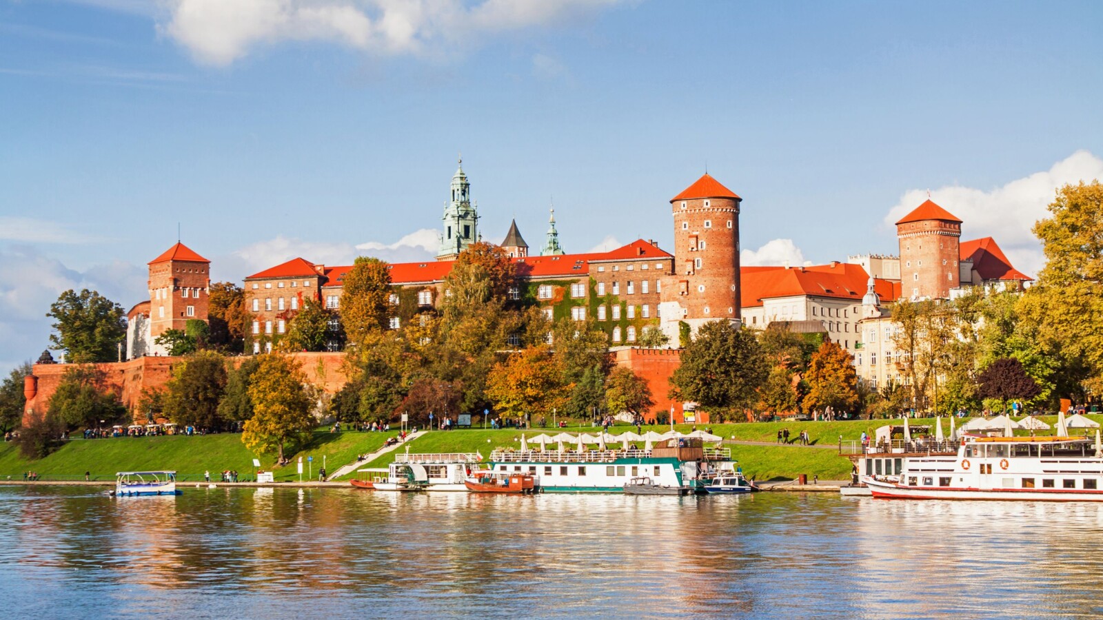 poljska-grad-krakov Wawelski dvorac u Krakovu, Poljska, s pogledom na rijeku Vislu, okružen jesenskim bojama i turističkim brodovima.