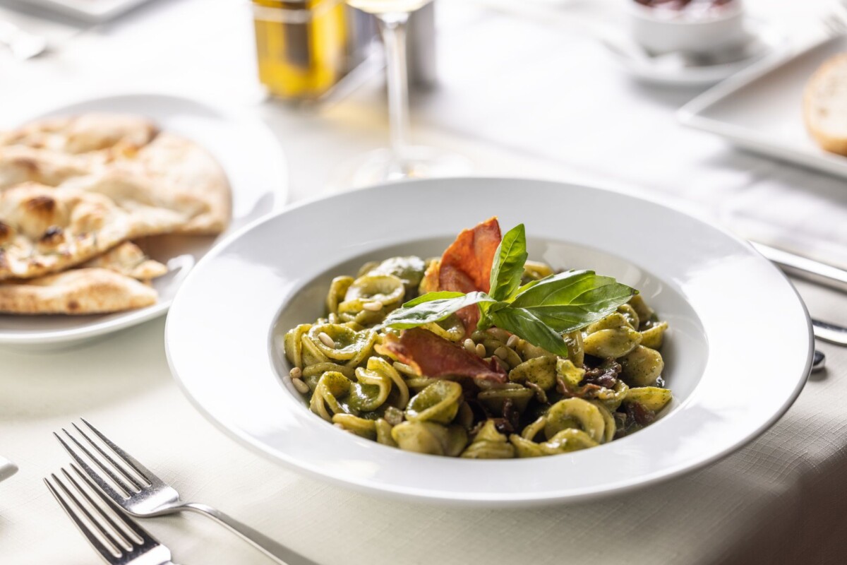 Tjestenina s pesto alla Genovese umakom, poslužena s listovima bosiljka i rajčicom, na elegantno postavljenom stolu