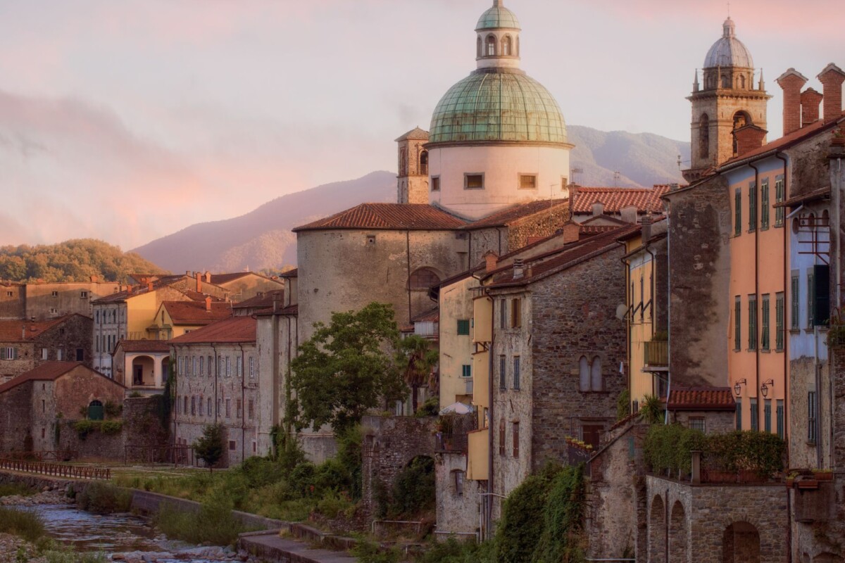 Romantični pogled na povijesni grad Pontremoli u Toskani, s kamenim kućama uz rijeku i impozantnom crkvom s kupolom u pozadini.