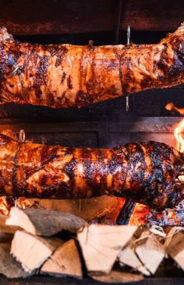 Ražanj s odojkom u vatri, okružen drvom za loženje u restoranu Bistro Europa kod Zagreba