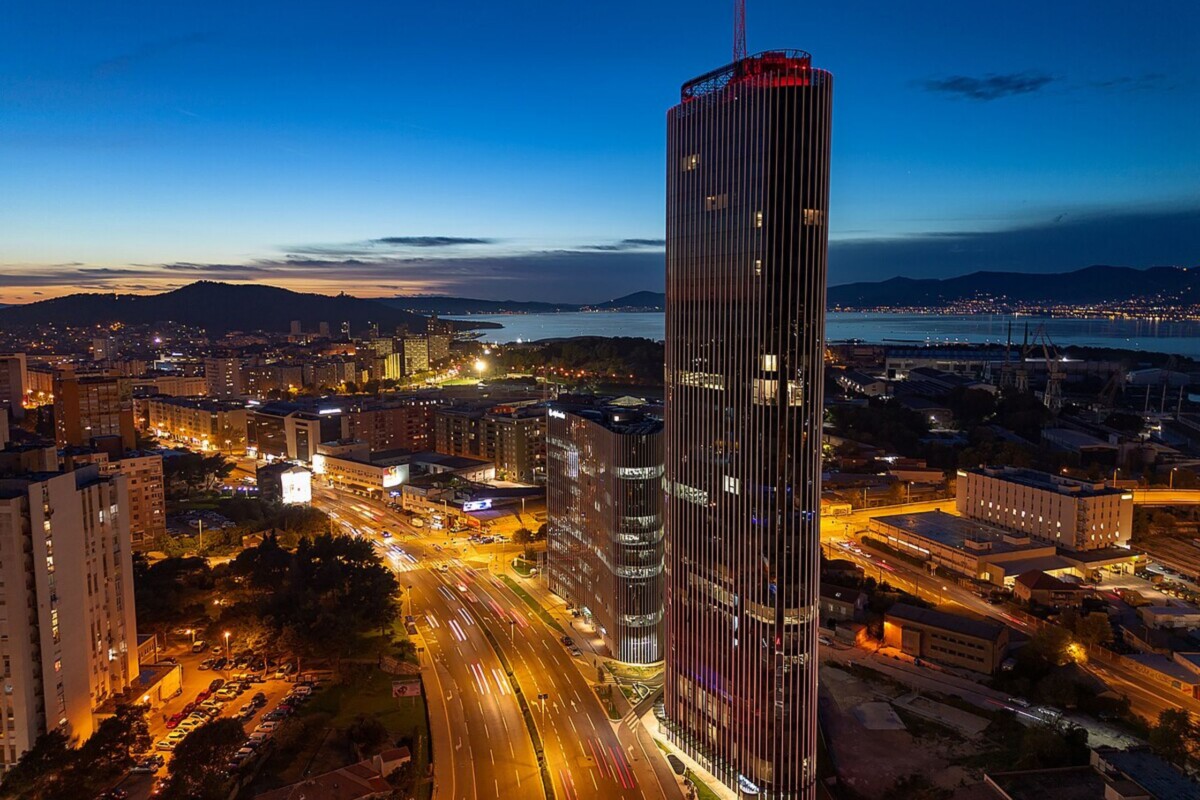 Pogled na Dalmatia Tower, najviši neboder u Hrvatskoj, u večernjim satima, s osvijetljenim prometnicama Splita i morem u pozadini.