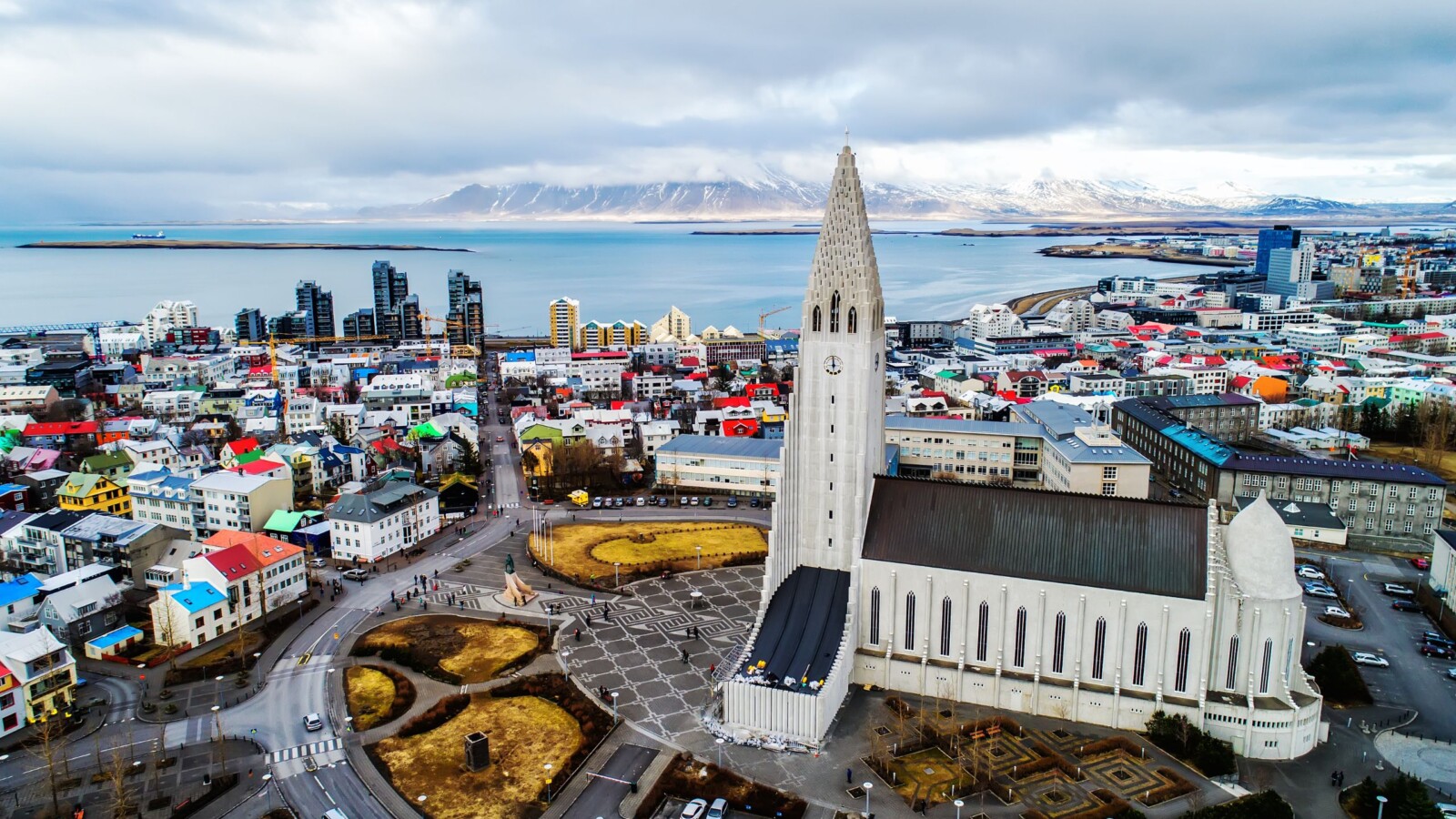 Pogled iz zraka na Reykjavik, slavni glavni grad Islanda, s impozantnom crkvom Hallgrímskirkja u prvom planu i snježnim planinama u pozadini.