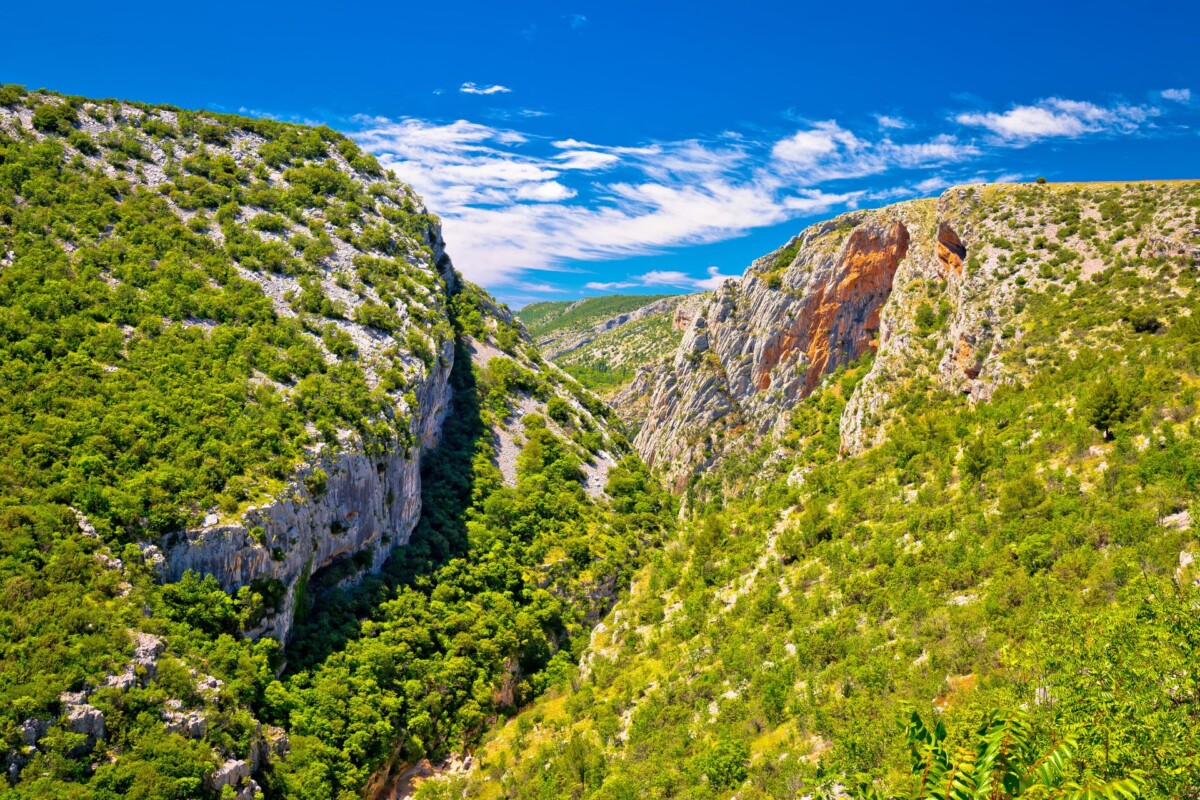 rijeka-čikola-okolica Impresivan kanjon s bujnom zelenom vegetacijom i strmim stijenama pod vedrim plavim nebom, dio dramatičnog krajolika u kojem se nalazi utvrda Ključica.