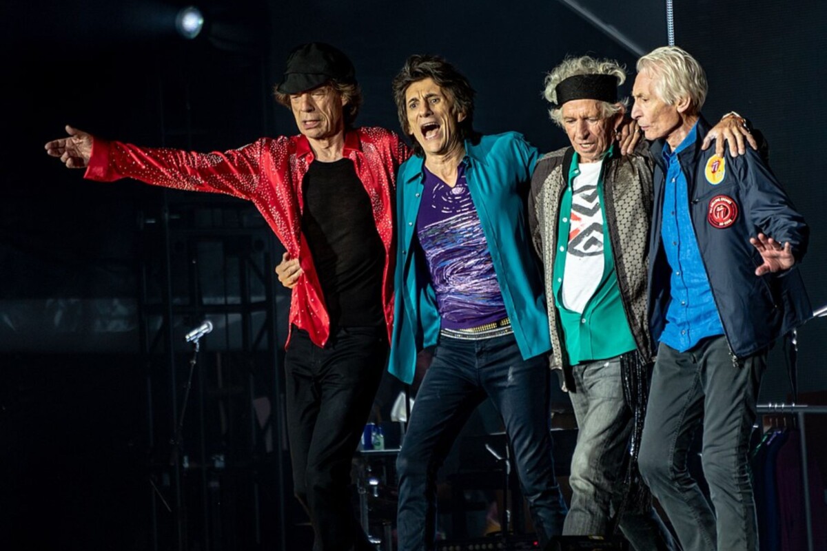 the-rolling-stones-clanovi-benda Članovi benda The Rolling Stones na pozornici tijekom koncerta, zagrljeni i nasmijani, odjeveni u šarene jakne i majice.