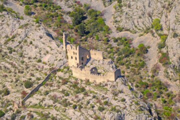 Pogled iz zraka na utvrdu Ključica, srednjovjekovnu tvrđavu smještenu na krševitom terenu, okruženu suhim, stjenovitim krajolikom s rijetkom vegetacijom.