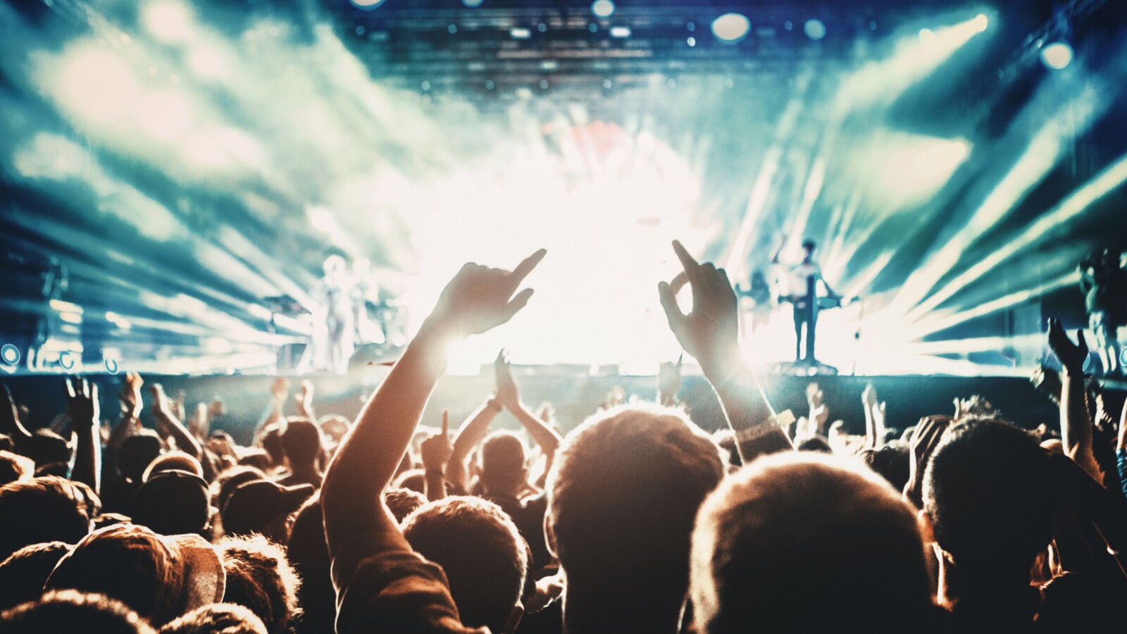 veliki-koncert Publika uživa na koncertu ispred osvijetljene pozornice, podignutih ruku i u euforičnom ozračju, dok svjetlosni efekti i dim stvaraju dramatičnu atmosferu na sceni.