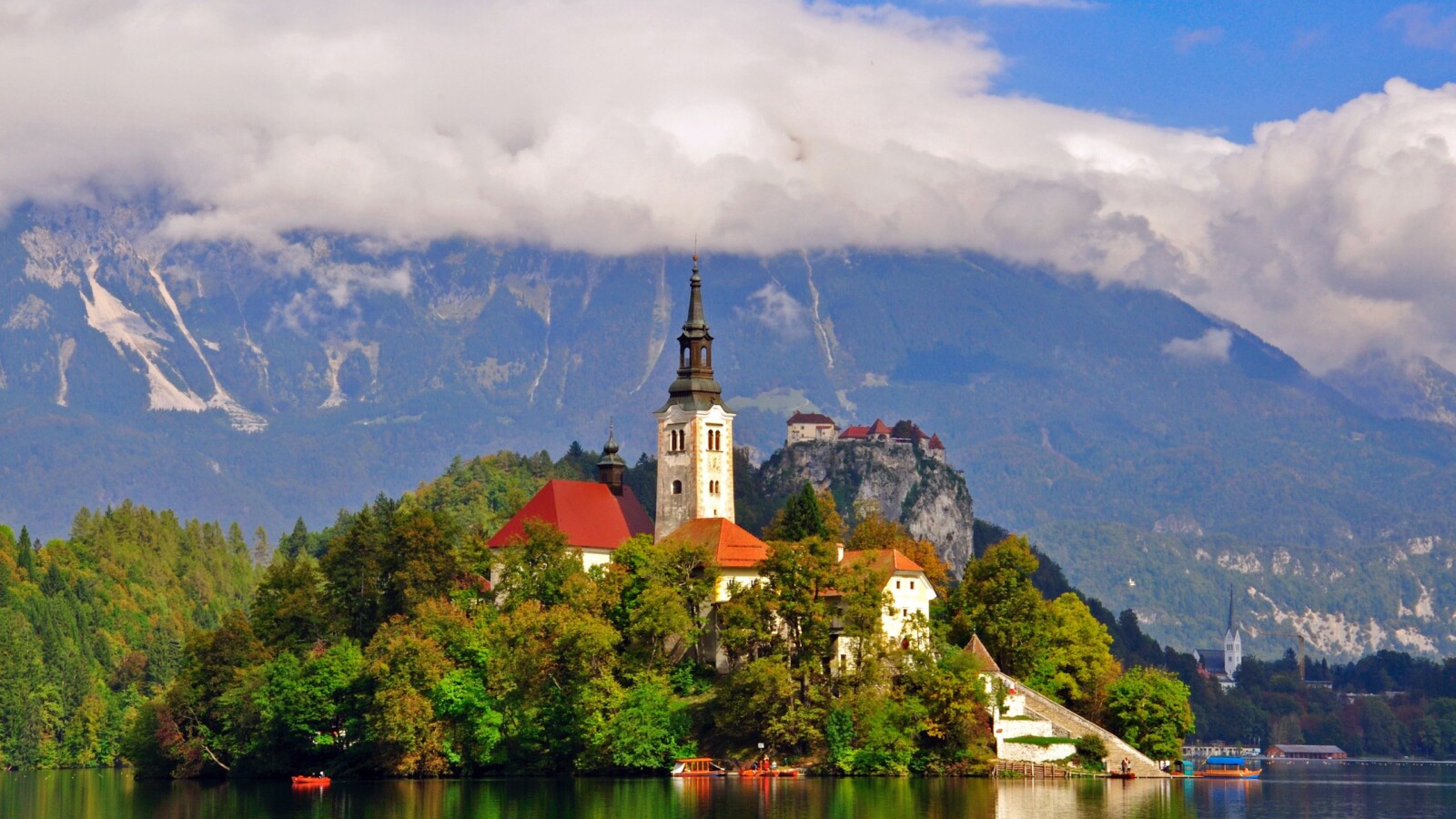 izlet-na-bled Otočić na Bledskom jezeru s crkvom Uznesenja Marijina, okružen jesenskim bojama i planinama u pozadini – čarobna slovenska destinacija u srcu prirode. Savršen izlet na Bled.