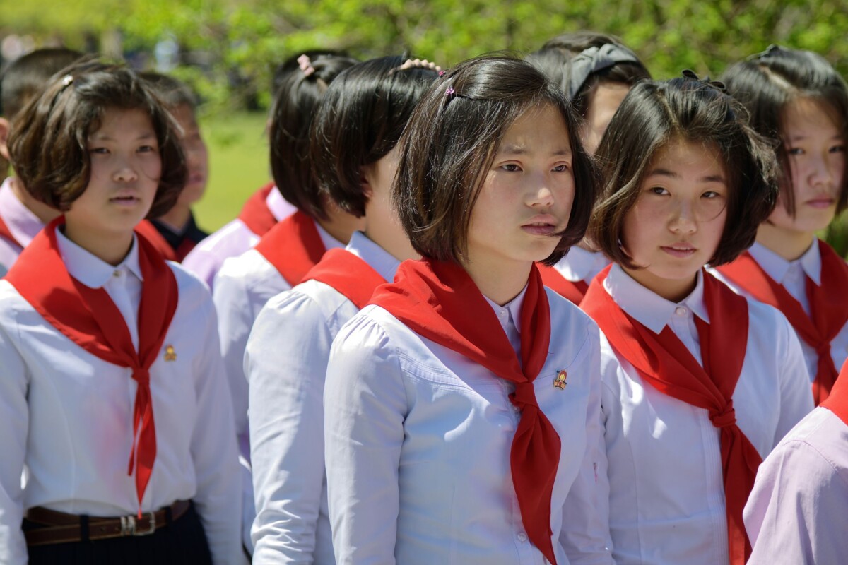 ljudi-u-sjevernoj-koreji Skupina sjevernokorejskih učenica u školskim uniformama s crvenim maramama i uredno podšišanim frizurama, stoje na otvorenom tijekom službenog događaja
