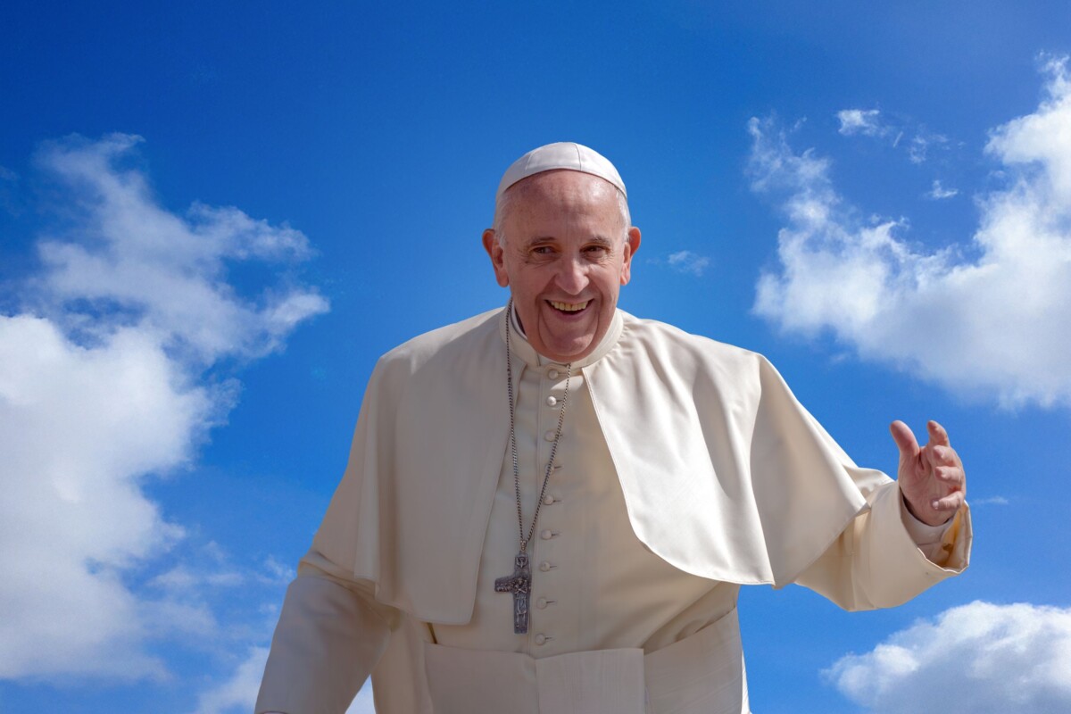 Papa Franjo nasmijan na otvorenom, u bijeloj papinskoj odori, ispred vedrog neba s oblacima.