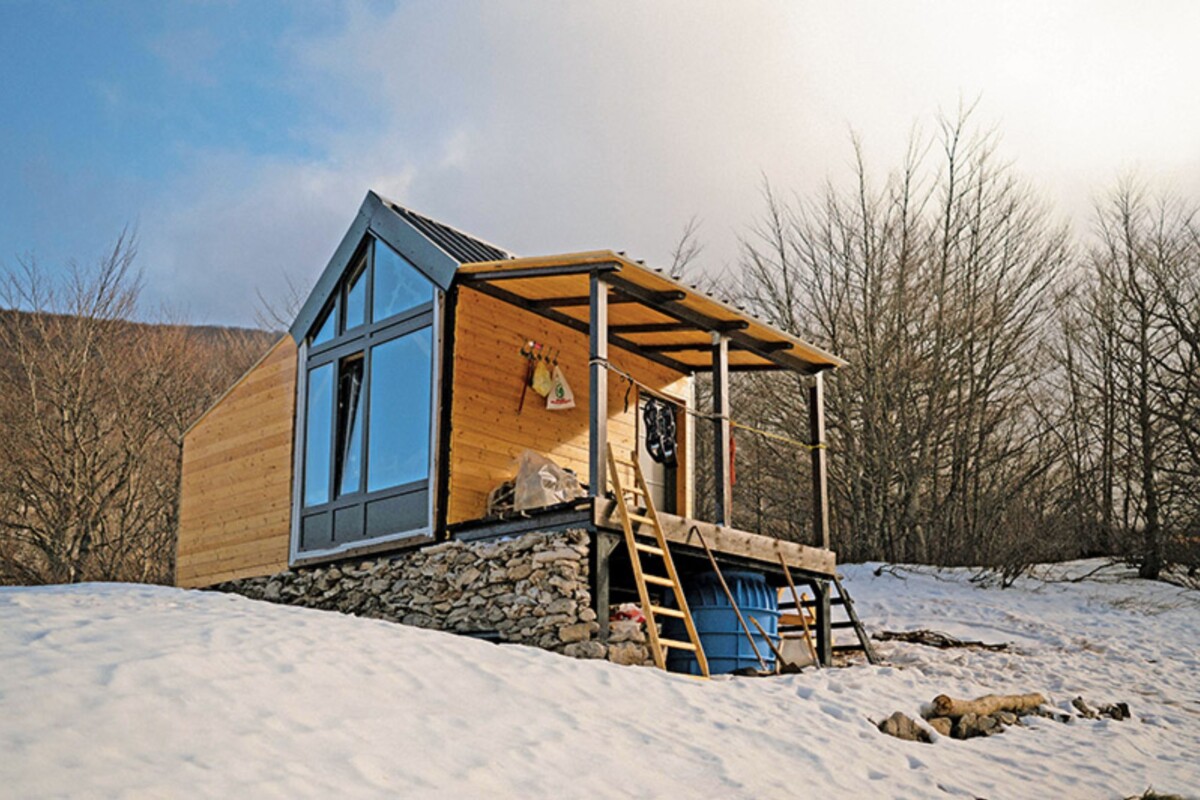 Planinarsko sklonište „Marko Novković“ na Velebitu, moderno drveno zdanje s velikim staklenim pročeljem, smješteno na snijegom prekrivenoj visoravni Rudine uz rub šume.