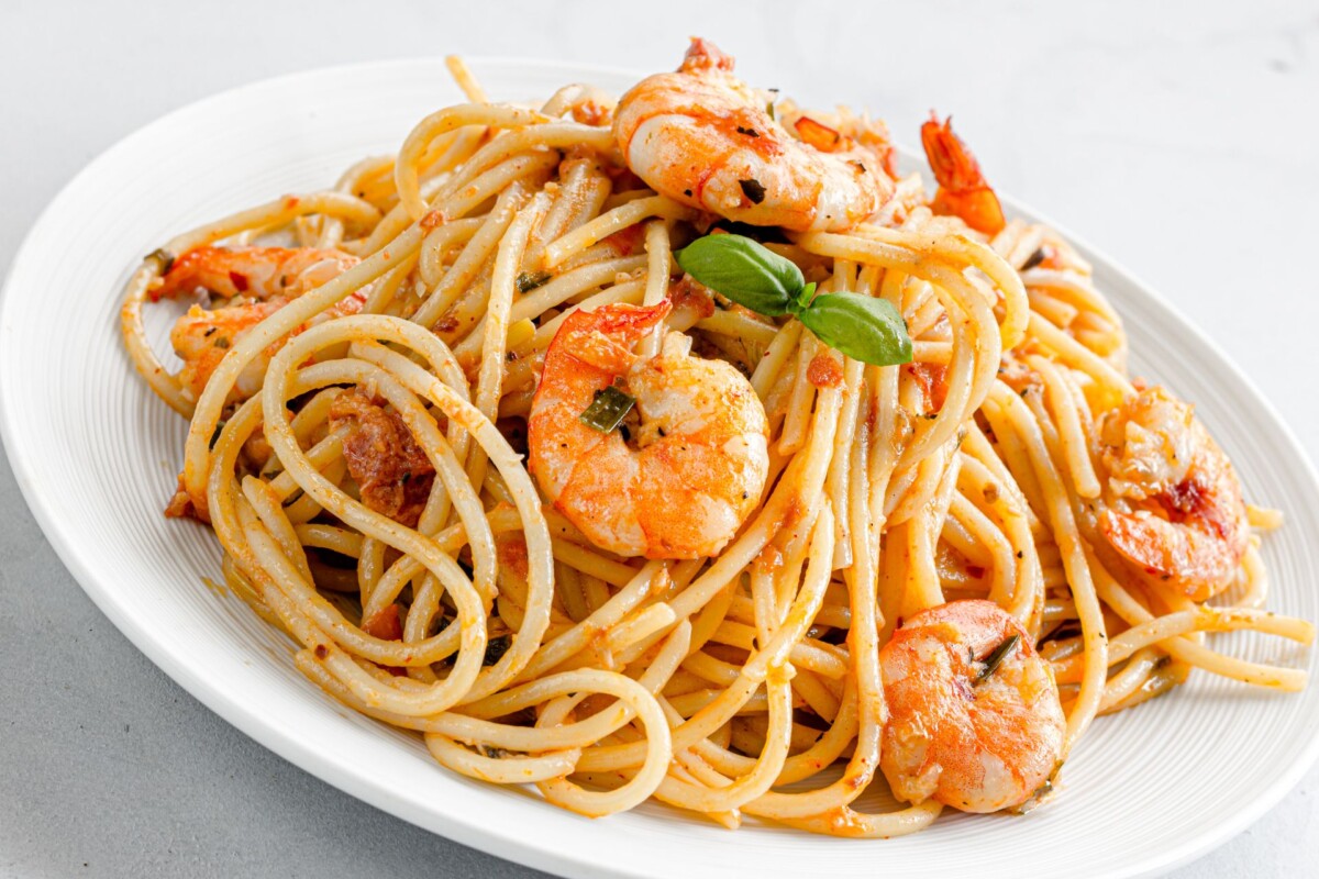 tjestenina-spageti-s-kozicama-na-crveno Servirani špageti s kozicama na bijelom tanjuru, ukrašeni listićem bosiljka