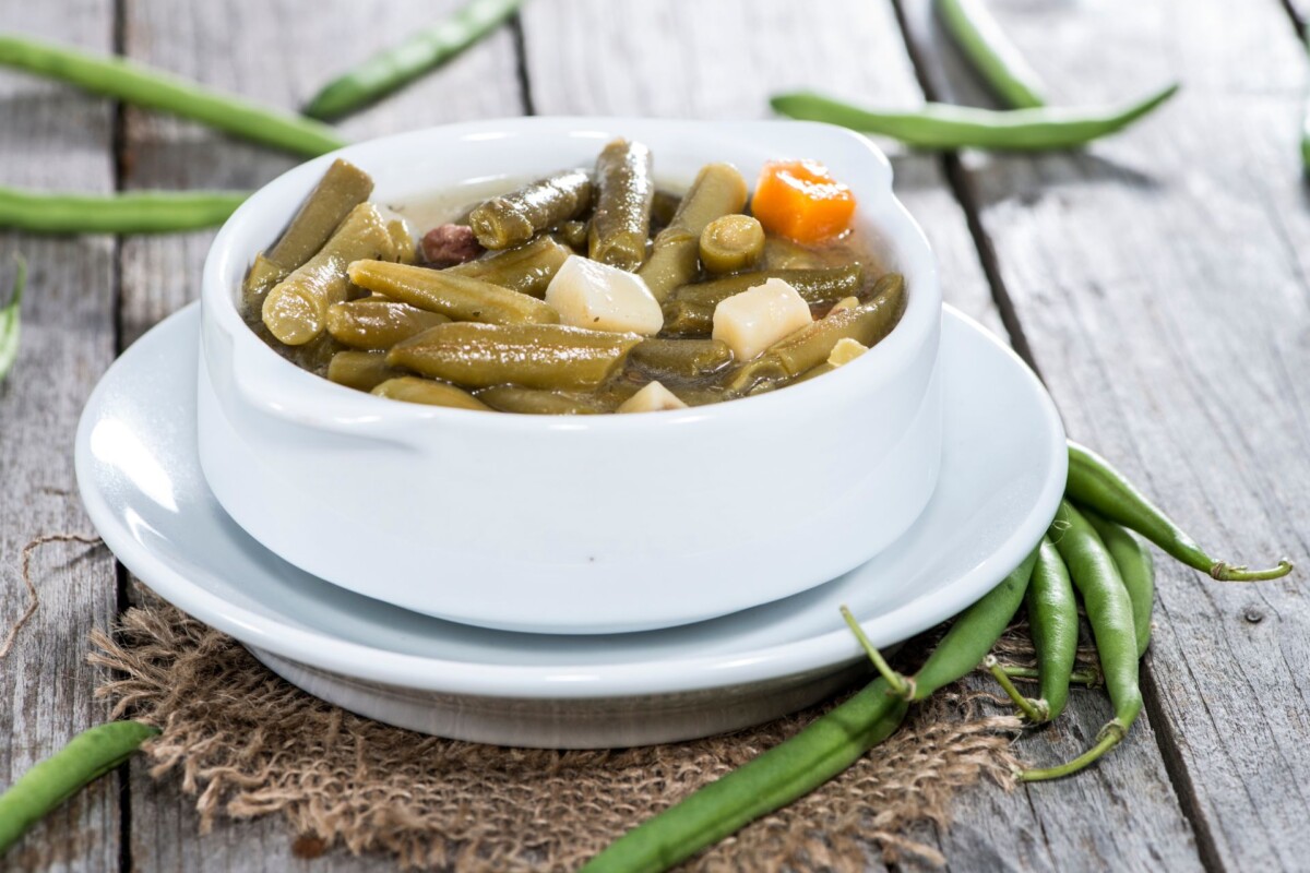 Vegetarijansko varivo od mahuna s mrkvom i krumpirom u bijeloj zdjeli na rustikalnom drvenom stolu – zdravo domaće jelo s mahunama.