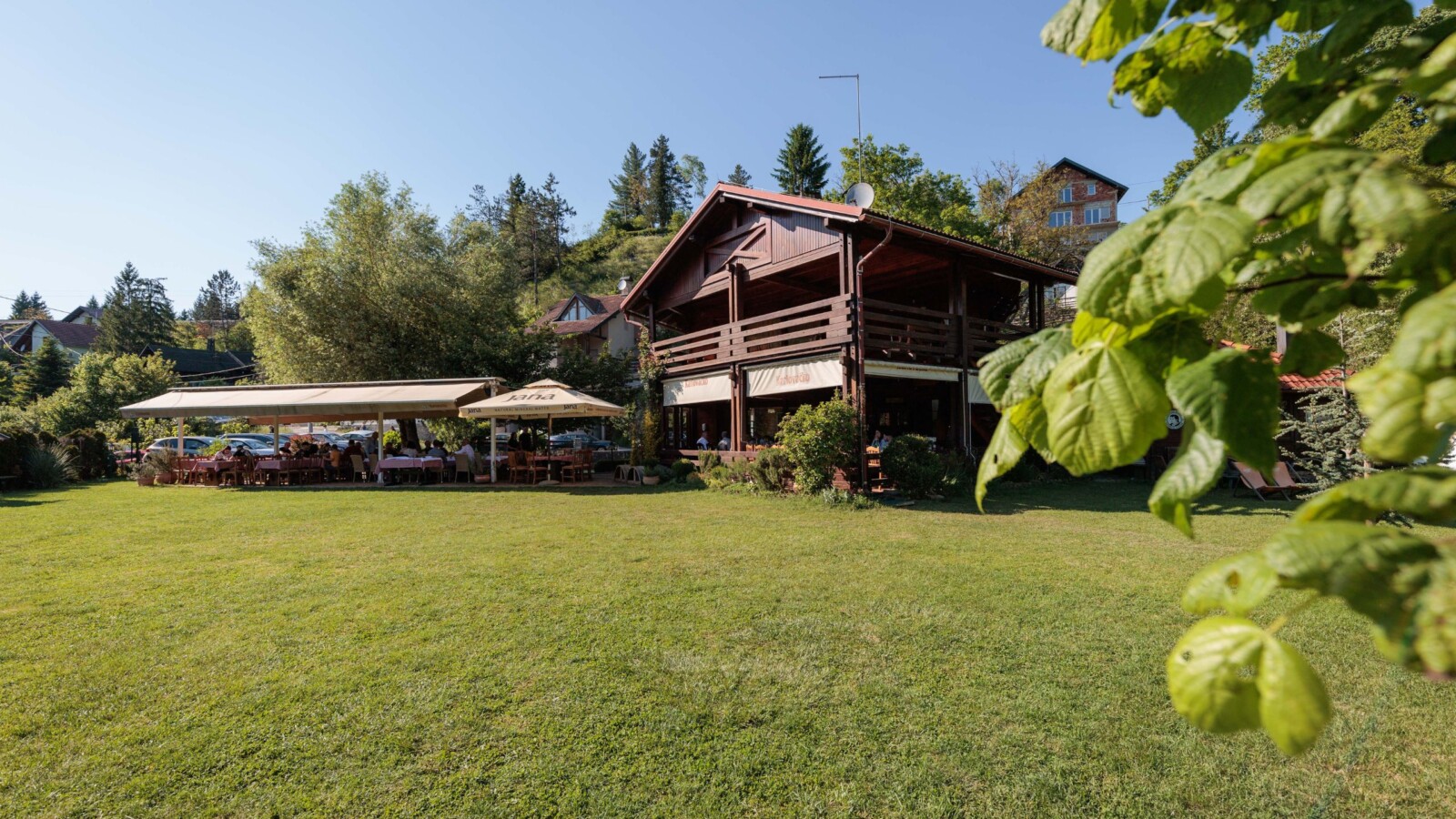 mreznicka-kuca-restoran Restorani na Kupi i Mrežnici – Mrežnička kuća s drvenom terasom i prostranim zelenim travnjakom uz rijeku, idealna za opuštanje u prirodi.