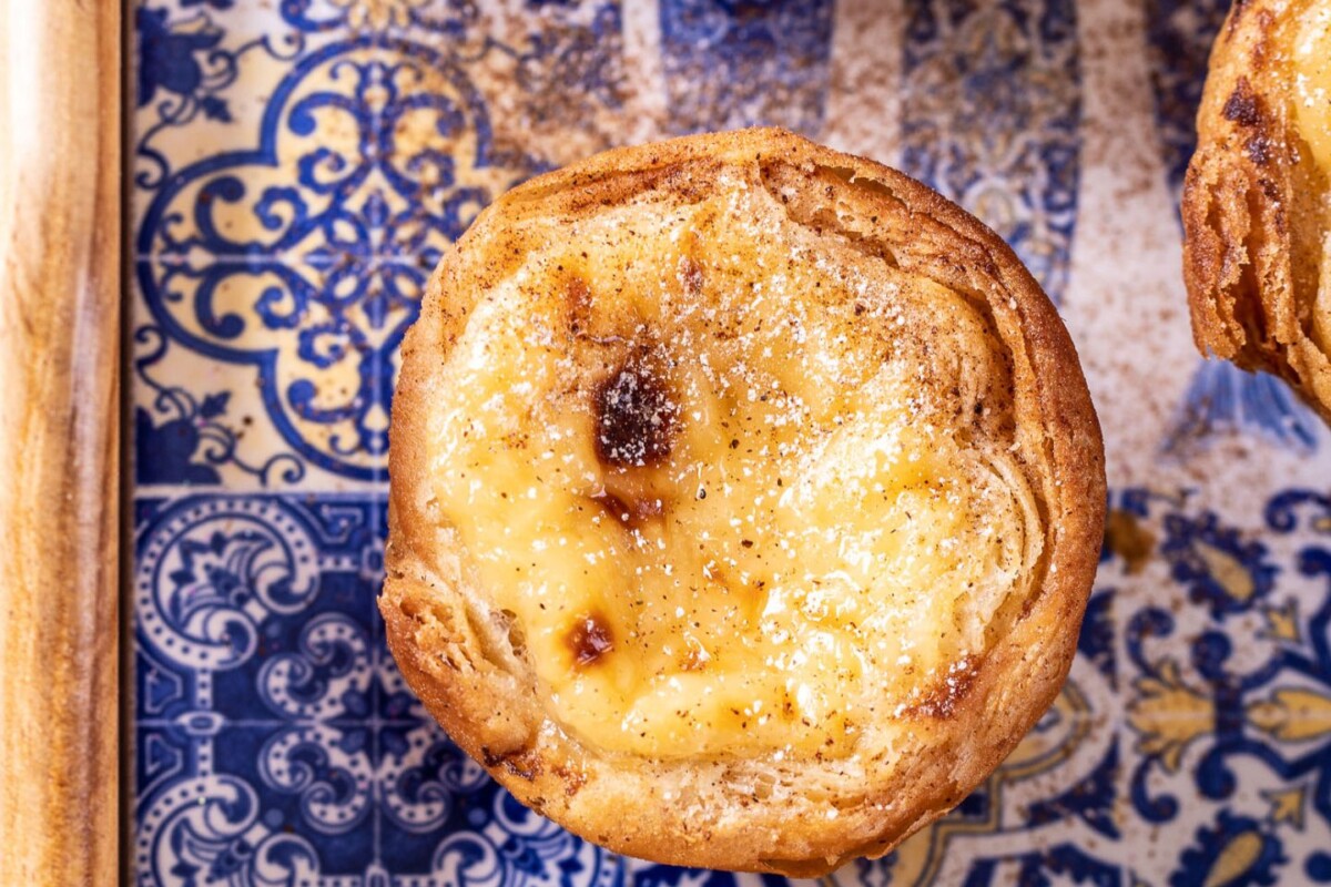 pasteis-de-nata Pastel de Nata (Pasteis de nata) posut šećerom na portugalskoj keramičkoj pladnju s plavo-bijelim uzorkom – autentična portugalska slastica iz Lisabona.