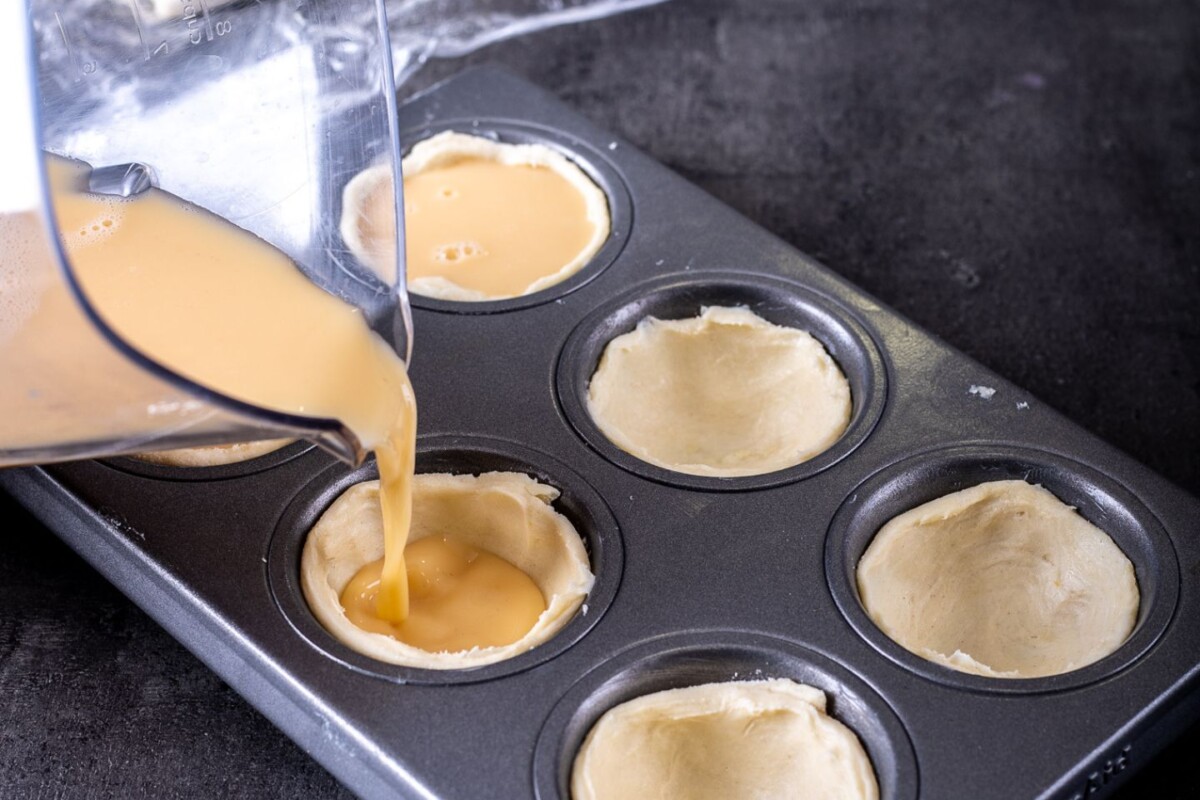 pastel-de-nata-priprema-7 Punjenje kalupa kremom za Pastel de Nata – tekuća krema se ulijeva u pripremljene podloge.