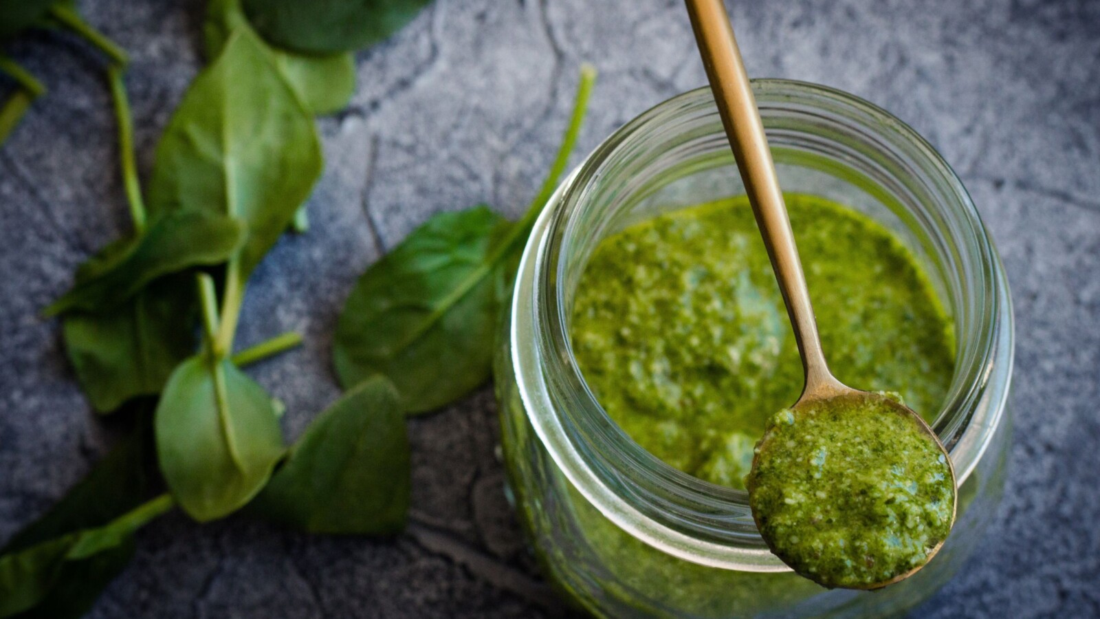 pesto-genovese Domaći pesto od bosiljka u staklenci s drvenom žličicom i svježim listovima sa strane