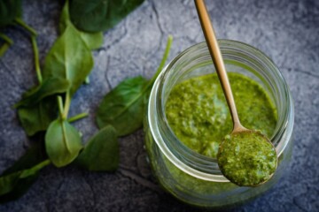 Domaći pesto od bosiljka u staklenci s drvenom žličicom i svježim listovima sa strane