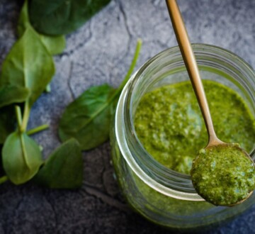 Domaći pesto od bosiljka u staklenci s drvenom žličicom i svježim listovima sa strane