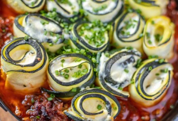 Zapečene punjene rolice od tikvica u umaku od mljevenog mesa, posute svježim vlascem, prikazane izbliza radi teksture i detalja.