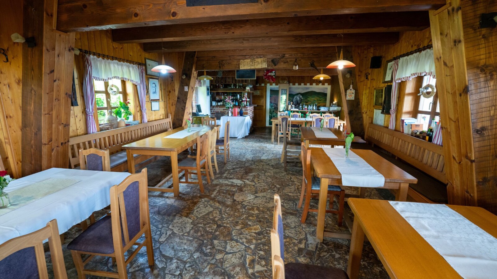 restoran-karlo-plesivica-1 Rustikalni interijer restorana Karlo na Plešivici s drvenim zidovima, kamenim podom i stolovima s bijelim stolnjacima u toploj, domaćoj atmosferi.