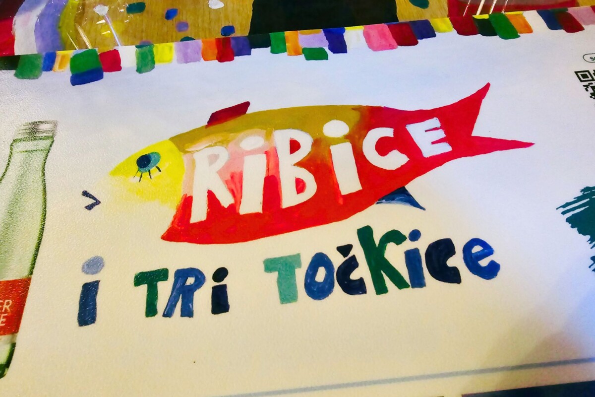 restoran-ribica-i-tri-tockice Ilustrirani logotip restorana Ribica i tri točkice s crvenom ribom i šarenim natpisom na podlozi stola.