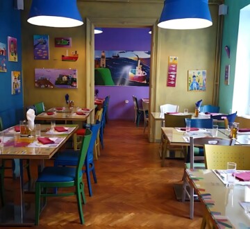 Interijer restorana Ribica i tri točkice s veselim, šarenim zidovima, ilustracijama i raznobojnim stolicama u toploj, opuštenoj atmosferi.