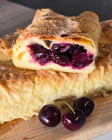 Pečena štrudla od trešanja s gotovim korama, narezana i poslužena uz svježe trešnje.