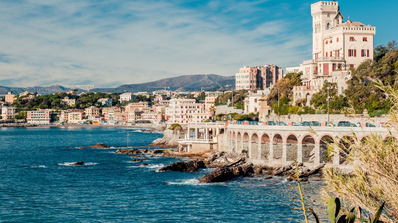 genova-italija Pogled na slikovitu obalu Genove s povijesnim vilama i zgradama uz more, okruženu azurnim Ligurskim morem i brdovitom pozadinom.