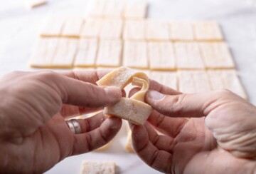 Ruka preklapa komad tijesta kako bi oblikovala karakterističan čvor kroštule. Recept za kroštule.