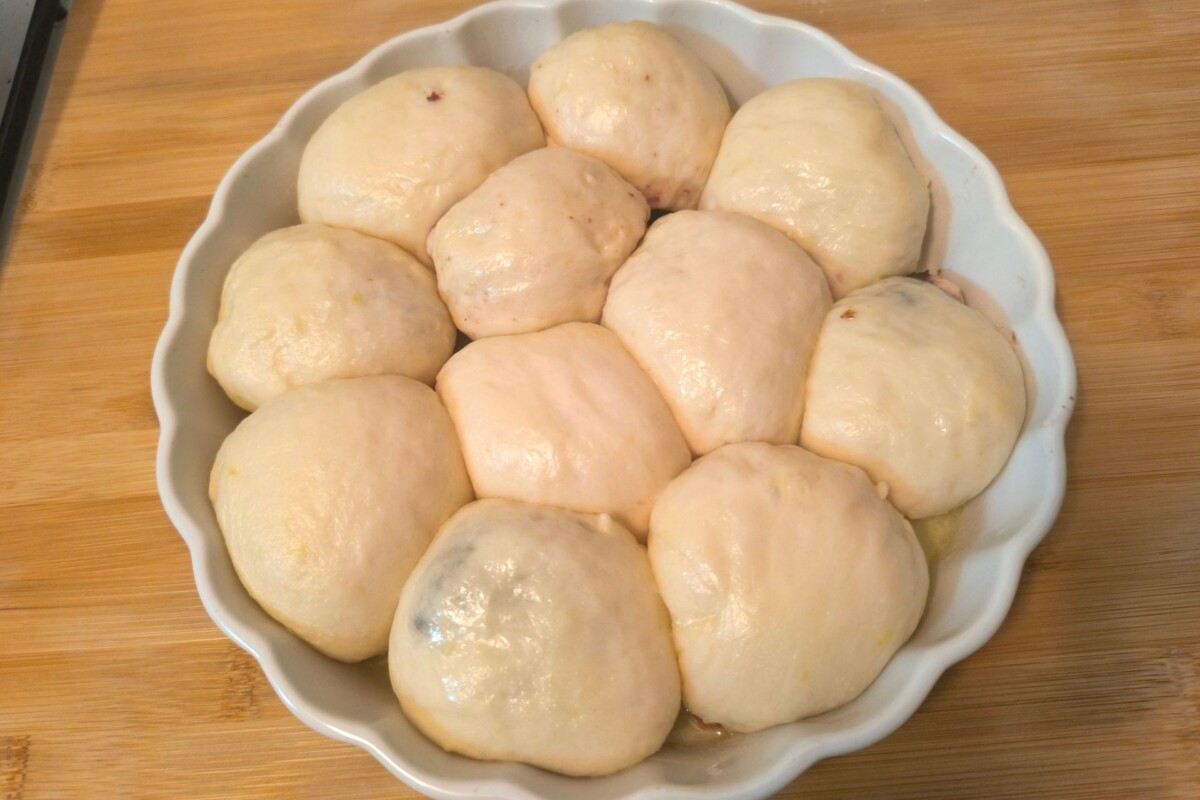Sirove buhtle posložene u okruglu keramičku posudu, spremne za pečenje, na drvenoj radnoj površini. Recept za najmekše i najbolje buhtle.
