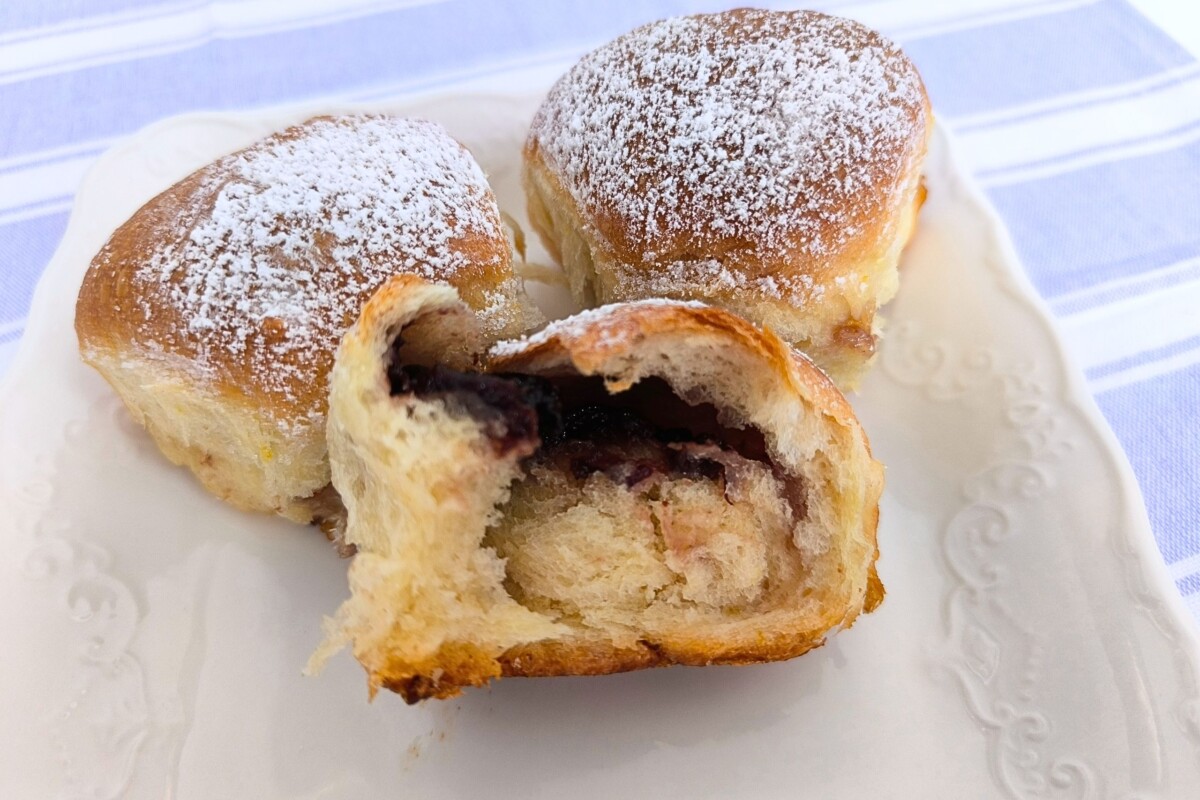 Tri domaće buhtle posute šećerom u prahu, jedna prerezana i otkriva mekanu unutrašnjost s tamnim voćnim džemom. Recept za najmekše i najbolje buhtle.