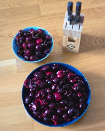 Zdjelice s opranim i očišćenim trešnjama pripremljene za izradu štrudle, uz bocu ekstrakta vanilije.