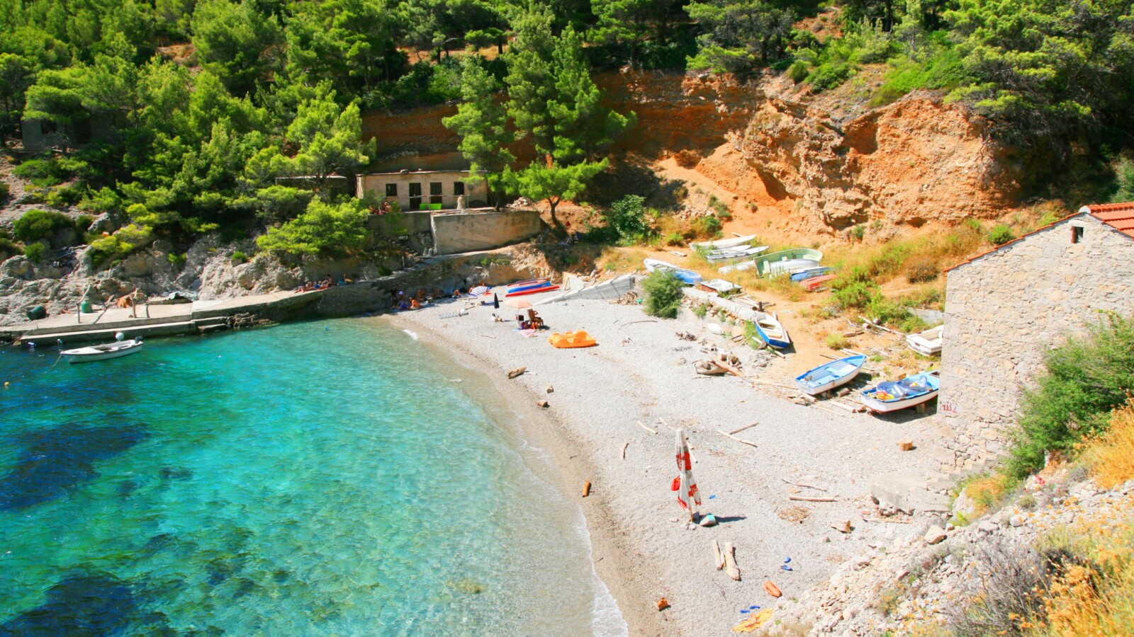 Plaža i uvala Sutmiholjska na otoku Mljetu s tirkiznim morem, šljunčanom obalom, čamcima i borovom šumom u pozadini