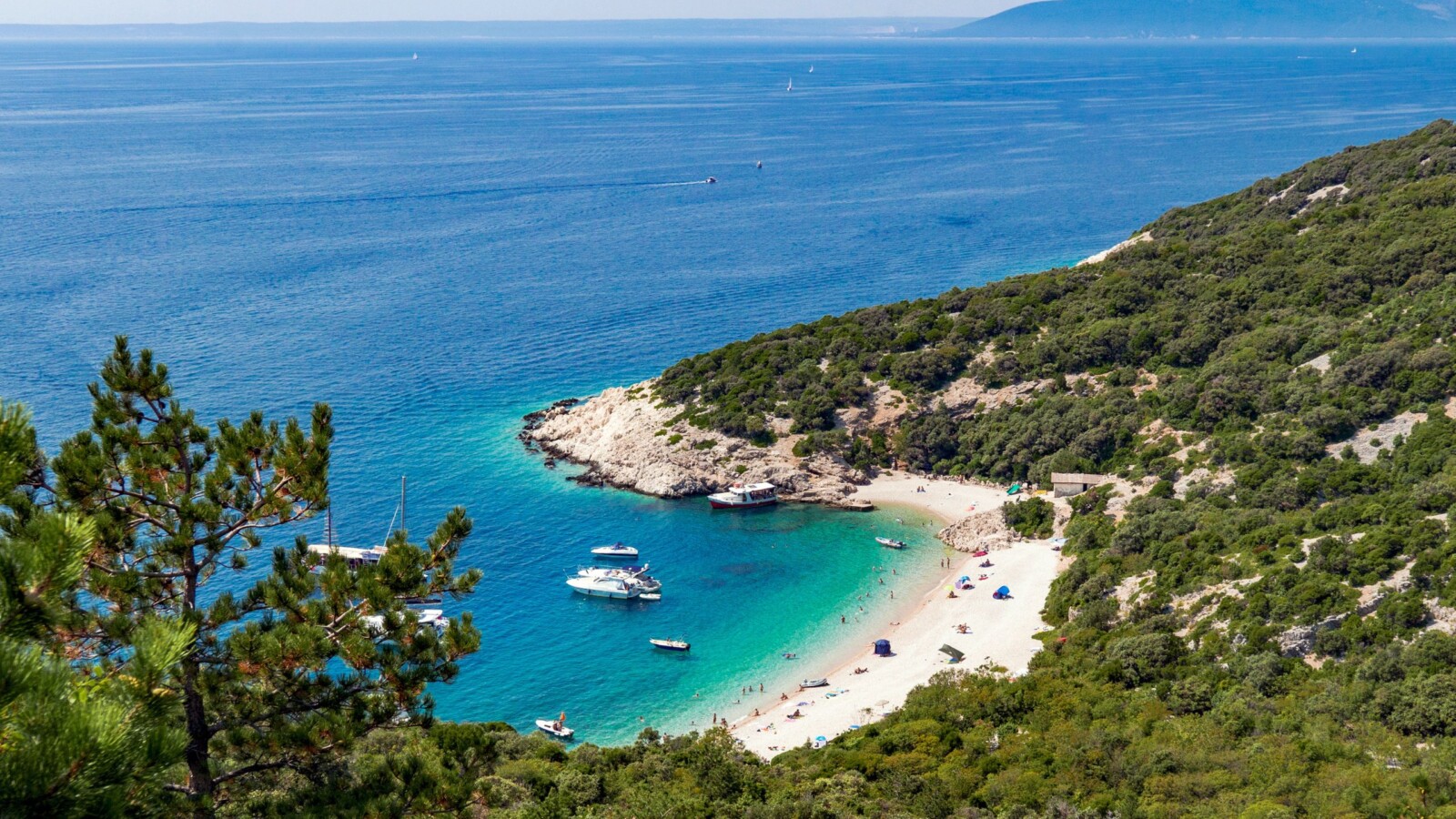 plaza-sveti-ivan-cres Pogled s visine na plažu Sveti Ivan ispod Lubenica na otoku Cresu, s tirkiznim morem, bijelim šljunkom, usidrenim brodovima i okruženjem guste mediteranske vegetacije.